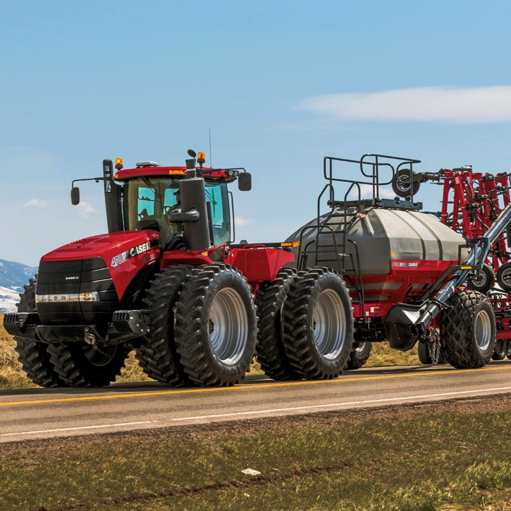 Case IH 470 Steiger pulling equipment down the highway with fields and mountains in the background 